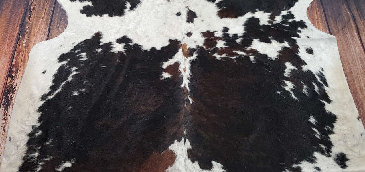 A gorgeous quality tricolored cowhide rug with a deep, soft brown, black, and white design.
