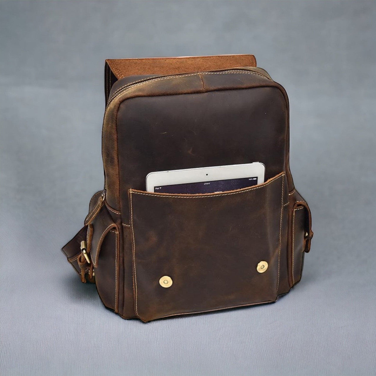 An overhead view of a leather backpack arranged against a backdrop of lush greenery, suggesting its suitability for outdoor excursions or nature-inspired adventures. The rugged yet sophisticated appearance of the backpack, with its durable leather construction and sturdy hardware, evokes a sense of exploration and wanderlust. The bag's spacious compartments and secure closures hint at its practicality for hiking, camping, or exploring the great outdoors.