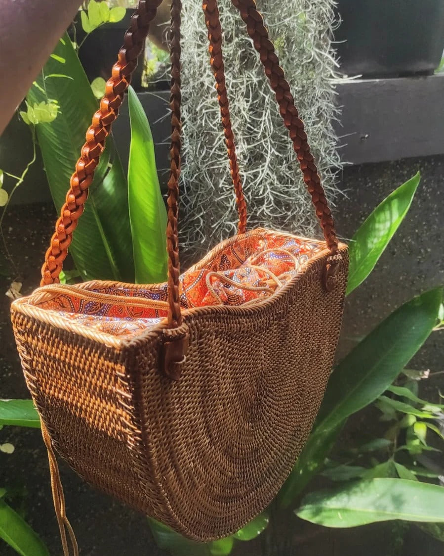 Zomerse rattan handtas met ronde onderkant en oranje voering, perfect voor strand of vakantie.
