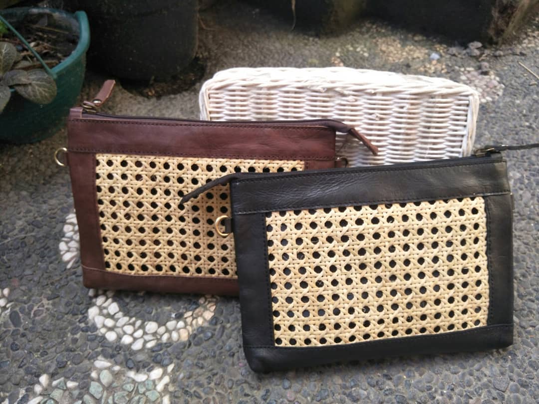 Geflochtene Rattan-Clutch mit braunem Lederrahmen auf Steinboden fotografiert