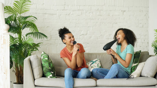 Two women singing into a microphone and hairdryer