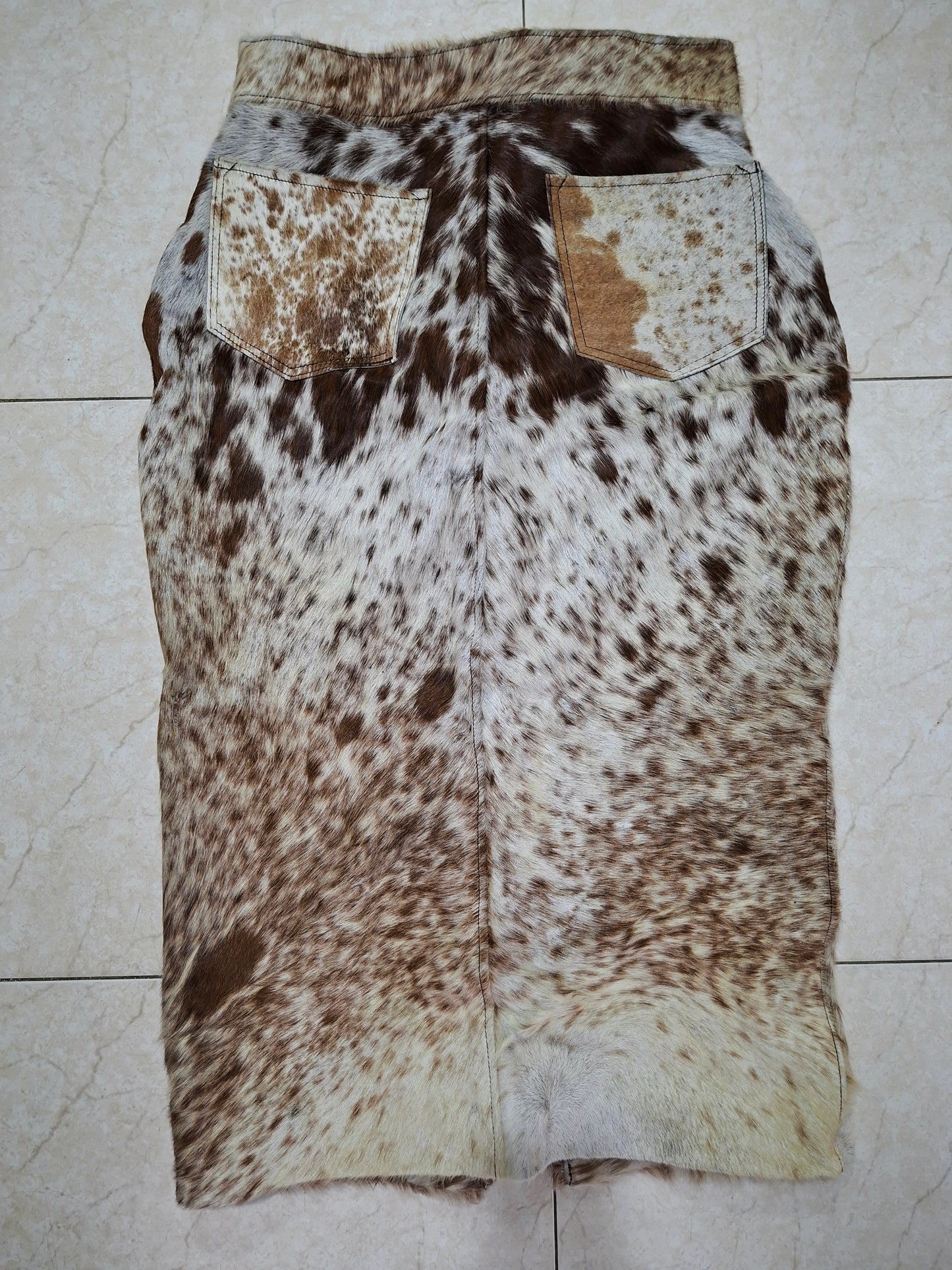 Detail van handgemaakte koeienprint rok met metalen knopen en stevige tailleband.

