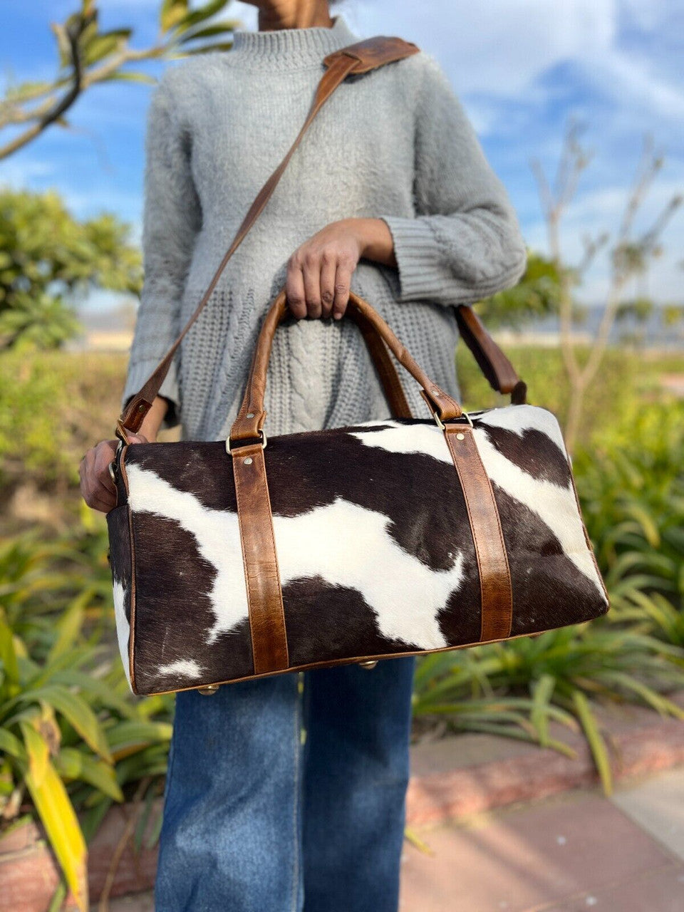 Durable cowhide travel bag displayed in a rustic outdoor setting.