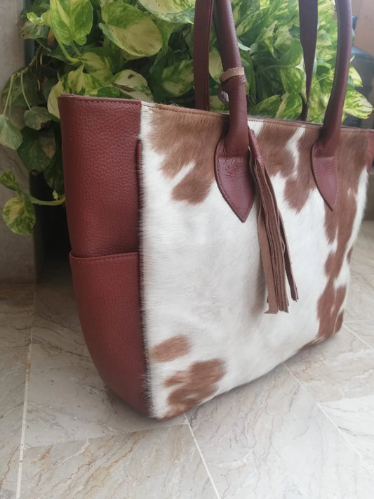 Brown and white cowhide shoulder bag for women featuring leather trim, zipper pockets, and roomy interior. Perfect cowhide purse with free shipping.

