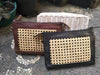 Geflochtene Rattan-Clutch mit braunem Lederrahmen auf Steinboden fotografiert

